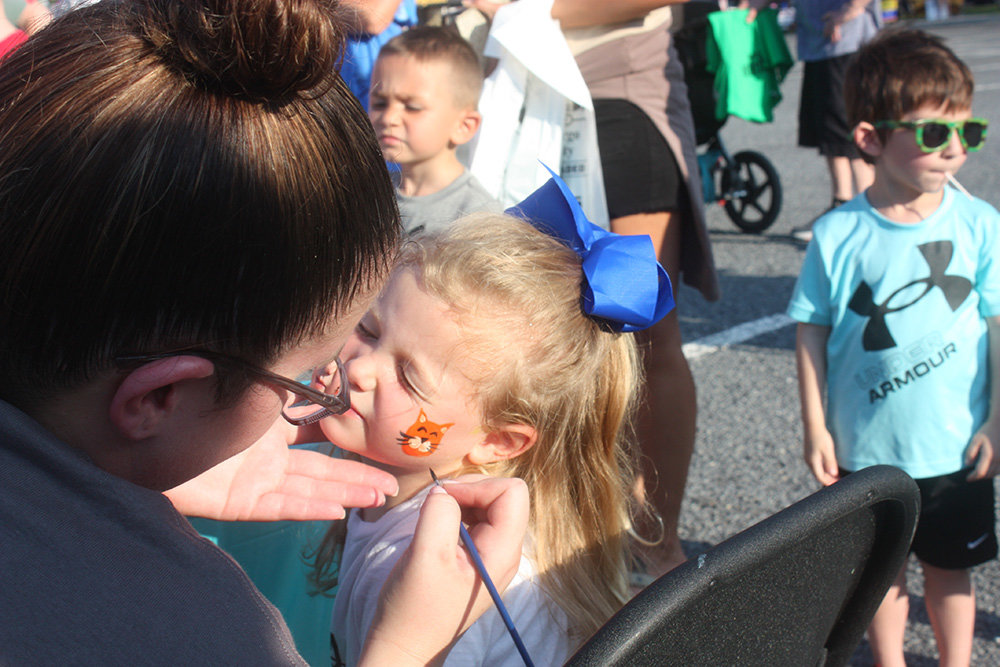 Emerson Stackpole, 3, has her face painted by Alicia Orozco of Uptiquing.