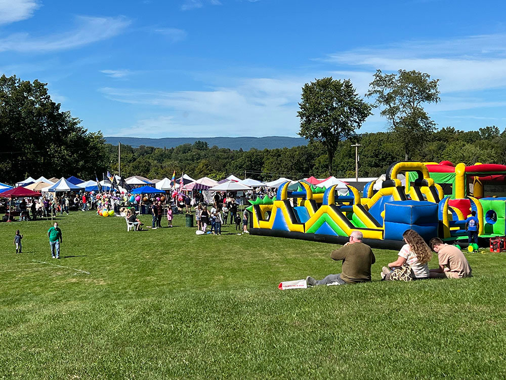 Festival visitors sit on the hillside to enjoy some food as more and more people arrive and walk around the vendor booths.
