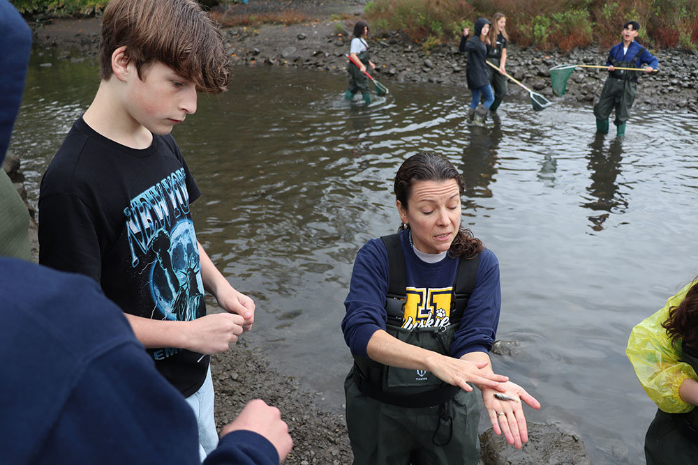 Grade 8 students from Highland Middle School, including Robert Donaldson (left), work together to identify a small fish held by Science teacher Cornelia Harris.