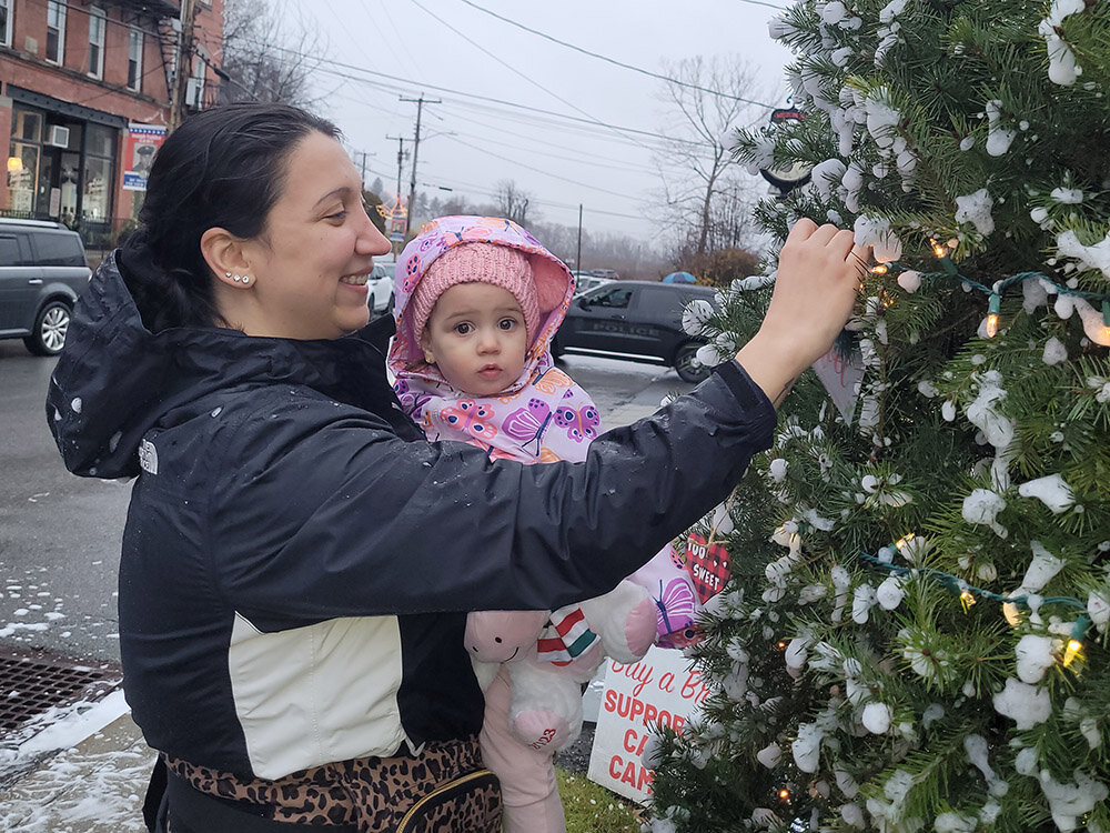 Anthoula Stekas helps daughter Elina hang an outdoor-friendly ornament on the Milton holiday tree, at the annual tree-lighting ceremony December 3.